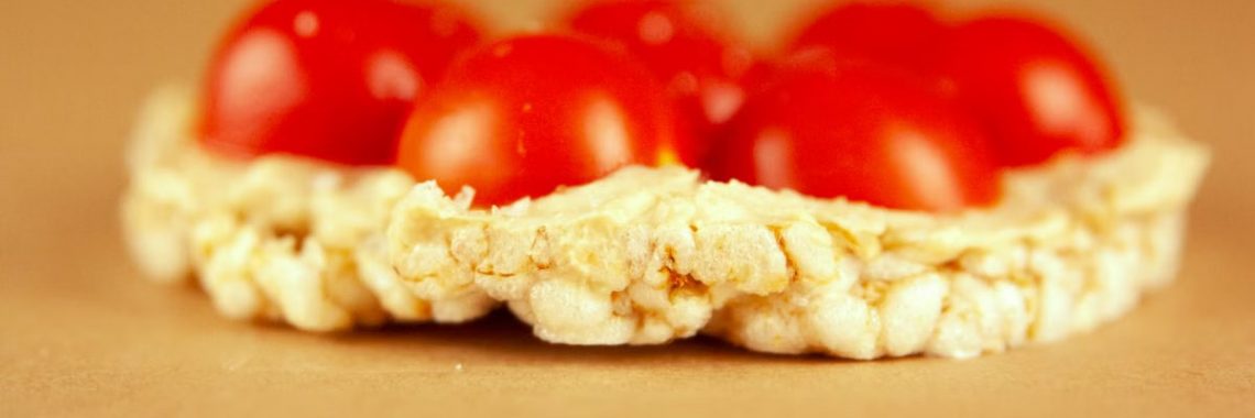 Macro shot of a rice cake topped with fresh cherry tomatoes on a warm background.