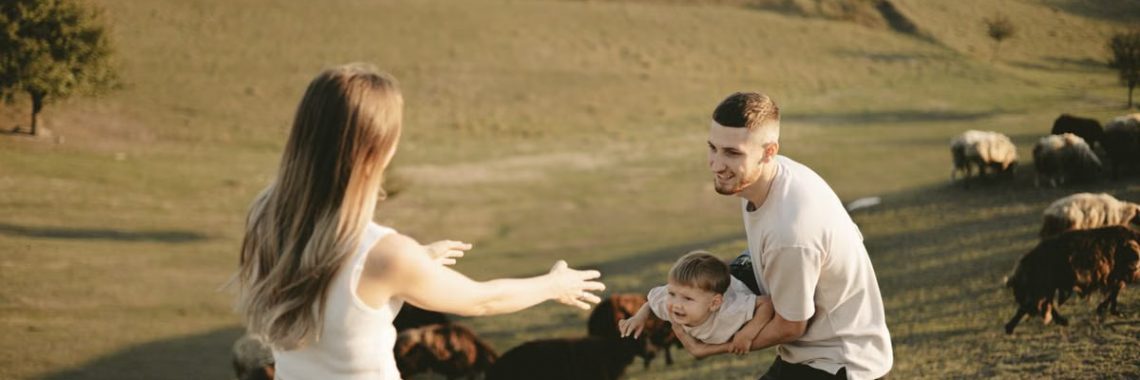 A joyful family with a child in a pastoral setting, embracing countryside life with grazing sheep.